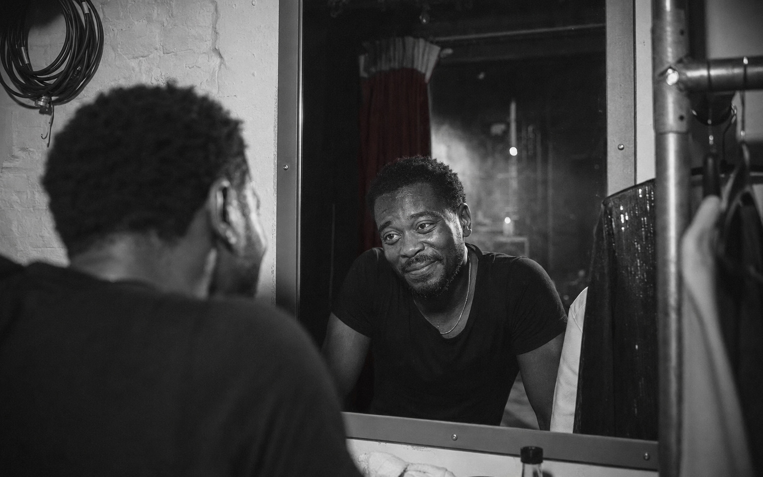 A performer alone backstage beneath a hard spotlight